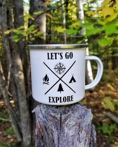 a white coffee cup with the words let's go explore on it sitting on top of a tree stump