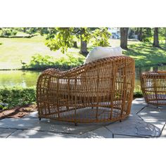 two wicker chairs sitting next to each other on a stone walkway in front of a pond