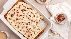 a pan filled with carrot cake next to two cups of coffee and spoons on a table