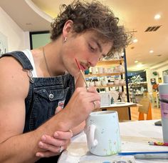 a man sitting at a table in front of a coffee cup with a toothbrush in his mouth