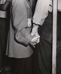 an old black and white photo of two people holding hands while standing next to each other