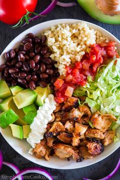 a white bowl filled with chicken, black beans, avocado and rice