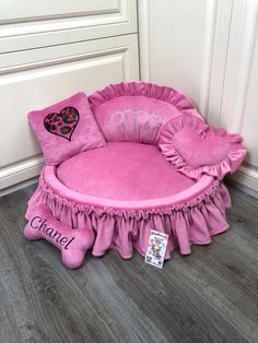 a pink dog bed with personalized pillows on the bottom, and a name tag attached to it