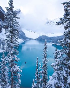 a lake surrounded by snow covered trees in the middle of a mountain range with blue water