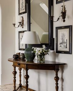 there is a table with flowers on it in front of a mirror and framed pictures