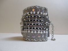 This beautifully detailed silver gray cuff measures from 7 inches to 9 inches with adjustable chain closure and is 2 3/8 inches wide. The base fabric is a dark silver lame with a lovely handmade center element. The entire piece is heavily hand beaded with coordinating element closures. Just beautiful! It is lined with a silver satin and lame ribbons. Love this! Very DECO! Adjustable Silver Cuff Bracelet With Rhinestones, Silver Adjustable Cuff Bracelet With Rhinestones, Silver Bling Cuff Bracelet For Evening, Adjustable Silver Bling Cuff Bracelet, Silver Adjustable Bling Cuff Bracelet, Silver Bling Adjustable Cuff Bracelet, Silver Cuff Bracelet For Party, Elegant Silver Beaded Cuff Bracelet, Adjustable Silver Cuff Bracelet For Evening