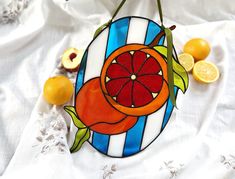 a stained glass ornament with oranges and lemons around it on a white table cloth