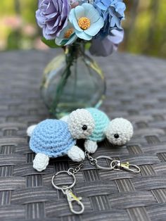 two crocheted turtle keychains sitting next to a vase filled with flowers