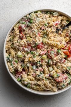 a bowl filled with pasta salad on top of a white table next to a black spoon