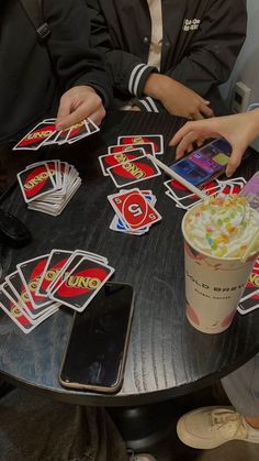 two people sitting at a table playing cards with drinks and cell phones in front of them