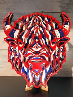 a red, white and blue bull head sculpture on a black table with wood planks in the background