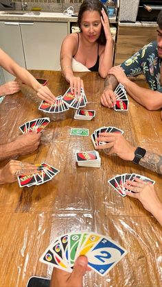 a group of people sitting around a wooden table playing card games on their cell phones