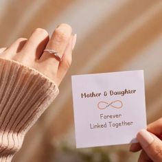 a woman holding up a card with a diamond ring on it that says mother and daughter forever linked together