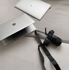 an open laptop computer sitting on top of a white bed next to a camera and lens