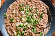 a bowl filled with beans and parsley on top of a wooden table next to a fork