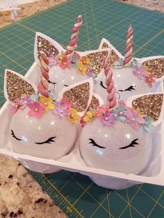 three unicorn - shaped cake pops are in an egg carton with gold glitter and pink flowers