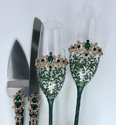 three wine glasses with green and gold designs on them next to a knife, fork and spoon