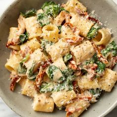 a white bowl filled with pasta and spinach covered in sauce on top of a marble table