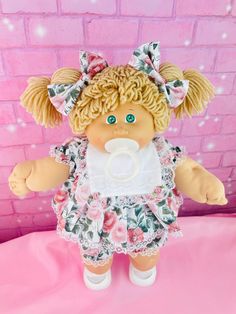 a doll with blonde hair and green eyes wearing a pink dress on a pink surface