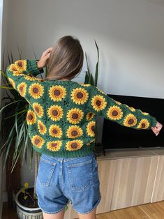 a woman standing in front of a tv wearing a sunflower sweater and denim shorts