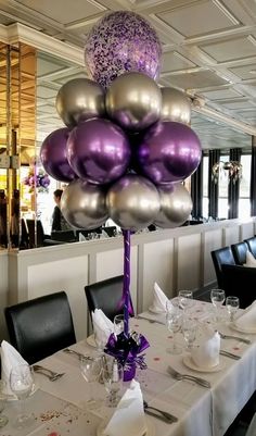 a table topped with lots of purple and silver balloons in the middle of a room