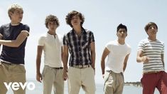 four young men standing next to each other near the ocean with their hands in their pockets