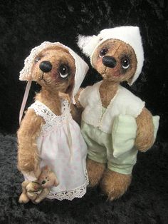 two teddy bears dressed in white clothes and bonnets, one holding a stuffed animal