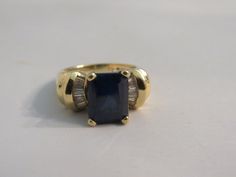 1.     Sapphire, Diamond, 14K Yellow Gold Ring – Size 7 ¼ Striking ring with a rectangular cut dark sapphire in the center and fanned diamonds on either side.  There is a lot of height to this yellow gold setting.  Stamped: 14K.  Dimensions: ¾” across the top and 1 1/8” overall (on the side top to bottom).  Size: 7 ¼.  6 grams/0.2 ounces. Rectangular Sapphire Ring In Yellow Gold, Dark Sapphire, Yellow Gold Setting, Yellow Gold Ring, Sapphire Diamond, Yellow Gold Rings, Gold Ring, Gold Rings, Jewelry Watches