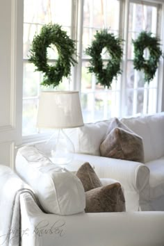 a living room with white furniture and wreaths on the window sill in front of it