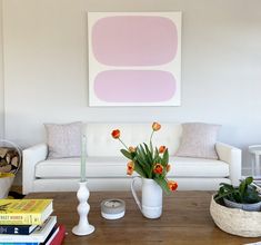 a living room with a white couch, coffee table and flowers in a vase on top of it