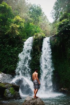 a man standing on top of a rock next to a waterfall in the jungles