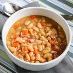 a bowl filled with beans and carrots on top of a striped cloth next to a spoon