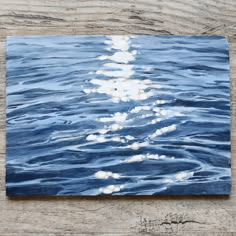 an acrylic painting of the moon rising over water on a wooden table top