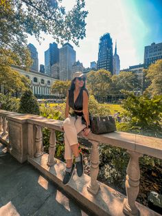 a woman sitting on top of a wooden bench in front of a cityscape