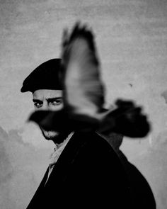 a black and white photo of a man with a bird flying in front of him