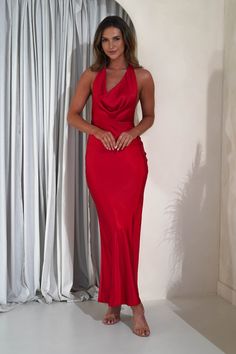 a woman in a red dress standing next to a white wall with curtains behind her