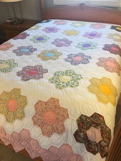 a bed with a quilt on top of it next to a night stand and lamp