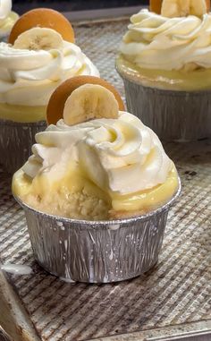 several cupcakes with banana slices and whipped cream in tin foil on a tray