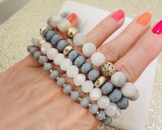 a woman's hand holding several bracelets with different colored beads and gold accents