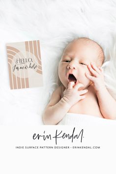 a baby yawns while laying on top of a white blanket next to a book