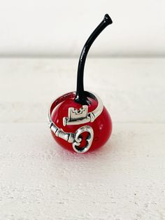 a small red apple with a black handle on it's side sitting on a white surface