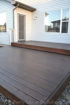 a large wooden deck in front of a white house with gravel and rocks around it