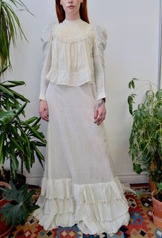 "Antique 1900's Victorian/Edwardian Two Piece Set. White Gauzy Cotton. Pleated Bib with Lace Trim. Princess/Mutton Sleeves. Inner Hidden Button Chest Closure. Side Waist Button Closure. Shoulder Button Closure. Long Unlined Skirt. Button Waist Closure. Layered Ruffle Hem. Feels like 100% Cotton Good/Fair Vintage Condition - Strong and wearable. Discoloration and spots throughout. Small part of lace trim on skirt ruffle is coming undone - simple repair. Fits XXS/XS Blouse Shoulder to Shoulder - 1 Prairie Dress With Ruffles For Daywear, Ruffled Prairie Dress For Daywear, Daywear Prairie Dress With Ruffles, Victorian Long Sleeve Dress With Buttons, Vintage White Victorian Dress With Ruffles For Daywear, Vintage White Victorian Day Dress With Ruffles, Victorian Daywear Dresses With Buttons, Victorian Long Sleeve Dress For Daywear, Victorian Style Long Sleeve Prairie Dress For Daywear