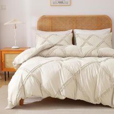 a bed with white comforter and pillows in a room next to a lamp on a table