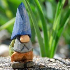 a small gnome figurine sitting on the ground next to some green plants and grass