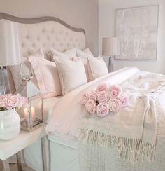 a white bed topped with lots of pillows and pink flowers next to a night stand