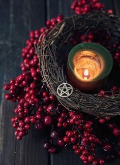 a candle sitting on top of a wooden table next to red berries and wicker