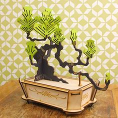 a wooden table topped with a vase filled with green paper cut outs and trees on top of it