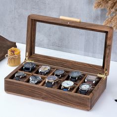 an open wooden watch box with twelve watches in it on a table next to a vase