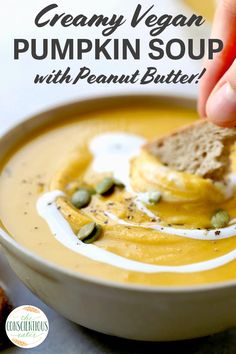 a person dipping some bread into a bowl of pumpkin peanut butter soup with pistachio sprinkles